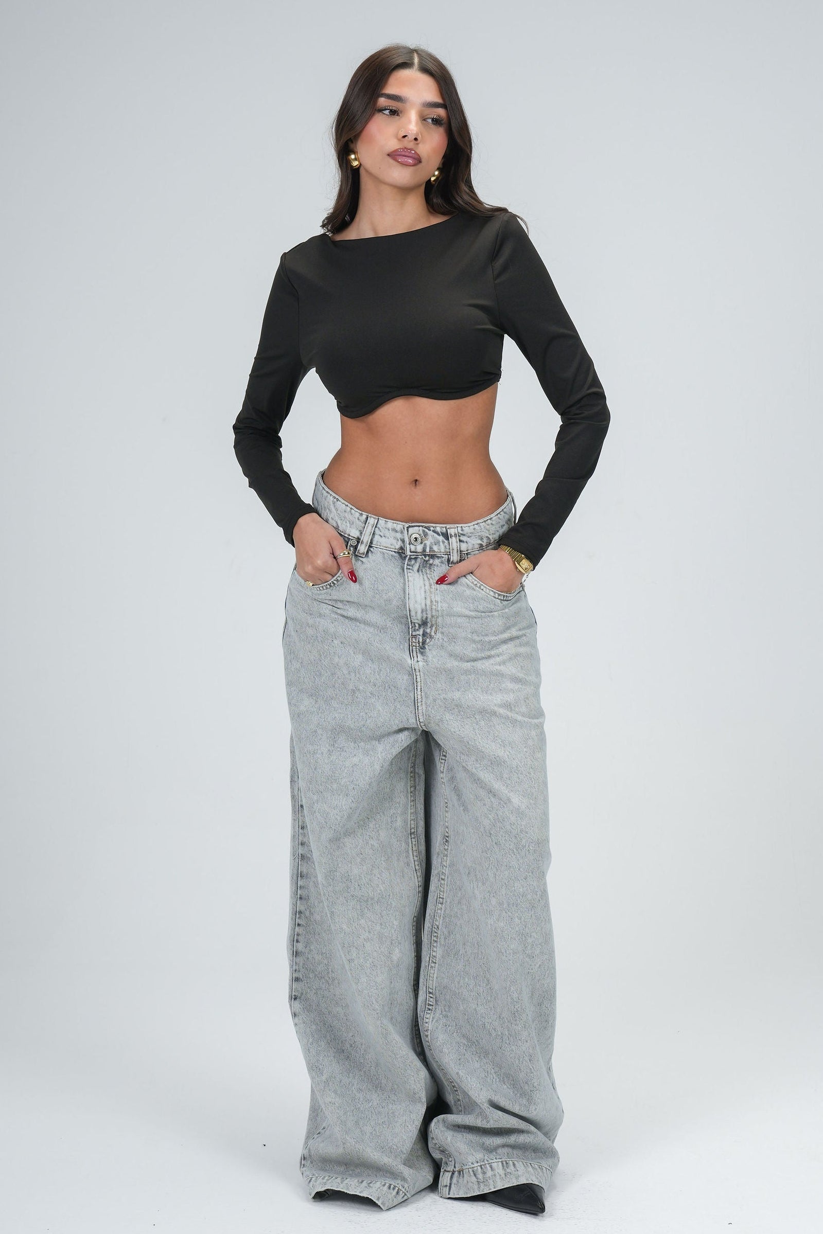 Woman wearing a black long-sleeve top and gray high-waisted jeans on a white background